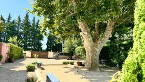 Un aparcamiento de grava con un banco, un árbol y un coche estacionado al fondo.