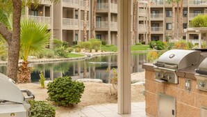 An outdoor kitchen area with multiple grills, a small pond, and a view of a multi-story building with balconies. - 2-bedroom resort in superb Indio with fitness room, AC. Enjoy relaxation (Indio)