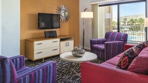 A hotel room with a TV, a minibar, a sofa, armchairs, and a view of a pool and mountains. - 2-bedroom resort in superb Indio with fitness room, AC. Enjoy relaxation (Indio)