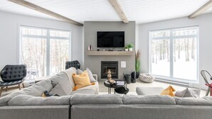 A modern living room with a fireplace, large windows, and a flat-screen TV. - Le Ô Calm |Spa| Hamac (Chertsey)