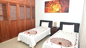 A hotel room with two beds, wooden wardrobe, and a colorful abstract painting on the wall.
