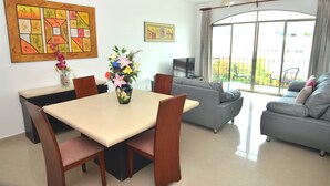 A dining area with a table, chairs, and a vase of flowers. There is a sofa and a television in the living area.