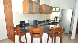 A kitchen with wooden cabinets, a stainless steel refrigerator, a microwave, and two wooden bar stools.