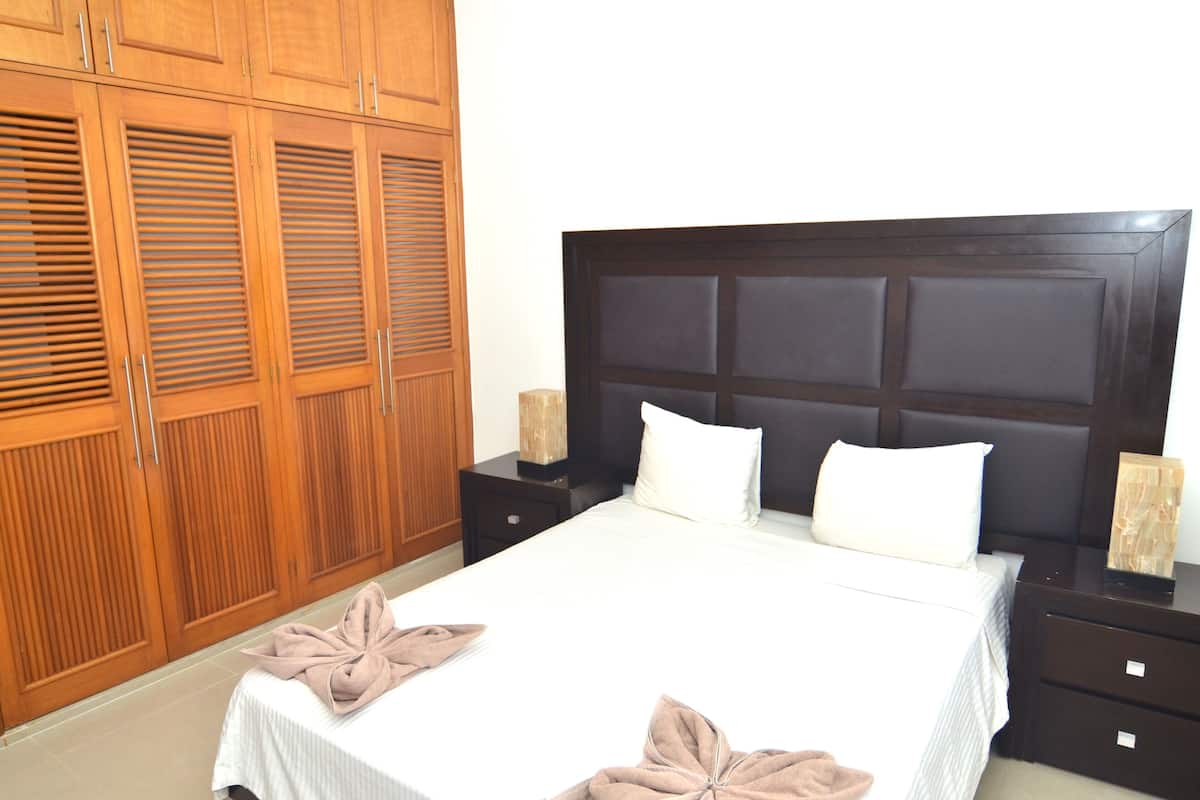 Una habitación de hotel con una cama grande, un armario de madera y dos mesitas de noche con lámparas.