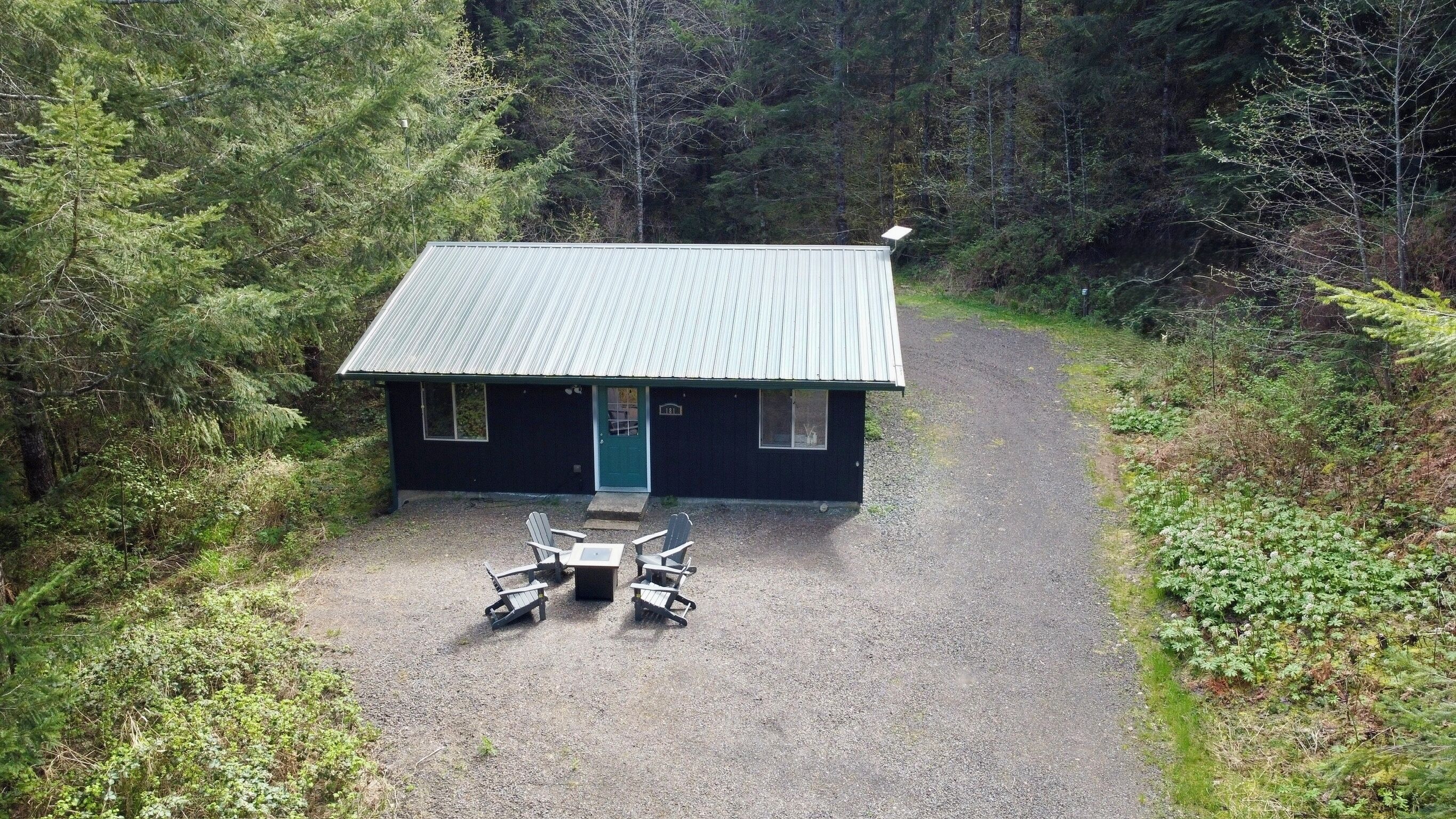 A small cabin with a gravel driveway and two Adirondack chairs in front.
