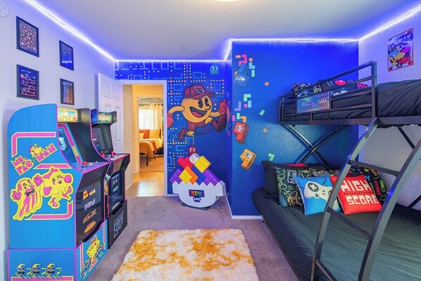 Une pièce avec un lit superposé, des jeux d’arcade, un jeu de Tetris et des décorations murales colorées.