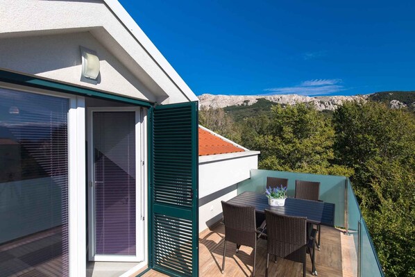 A balcony with a table and chairs, overlooking a mountainous landscape.