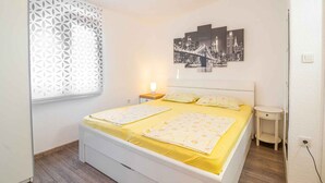 A bedroom with a bed, a nightstand, a wall-mounted cityscape picture, and a window with a geometric pattern. - Holiday apartment mit Balkon (Baška)