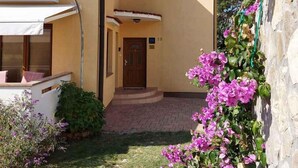A two-story building with a yellow facade, a visible entrance, and a small garden area with purple flowers. - Holiday apartment mit Balkon (Baška)