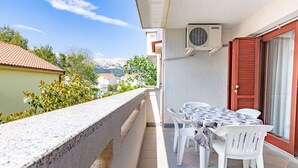 Un balcon avec une table et des chaises, un appareil de climatisation et une vue sur les bâtiments et les montagnes environnants.