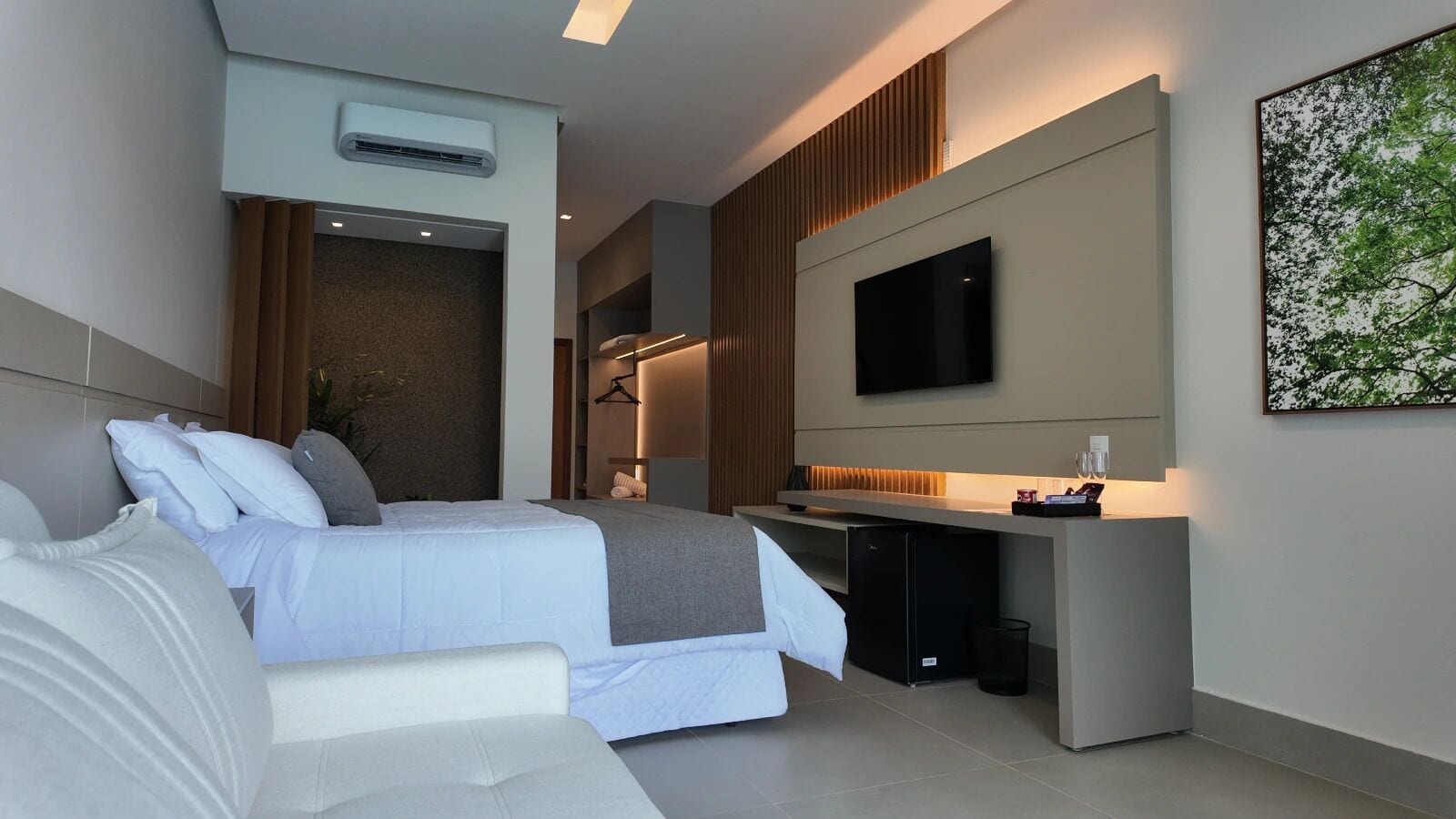 Quarto de hotel moderno com uma cama, um sofá, uma escrivaninha e uma televisão.