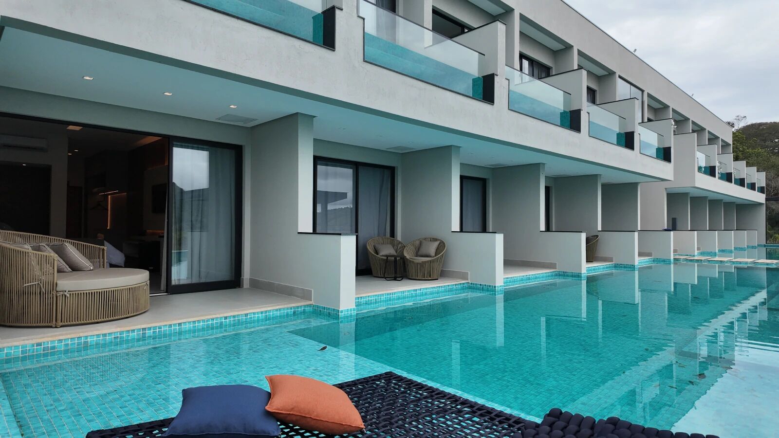 Een modern hotel met een zwembad, terras en balkon met glazen hekwerk.