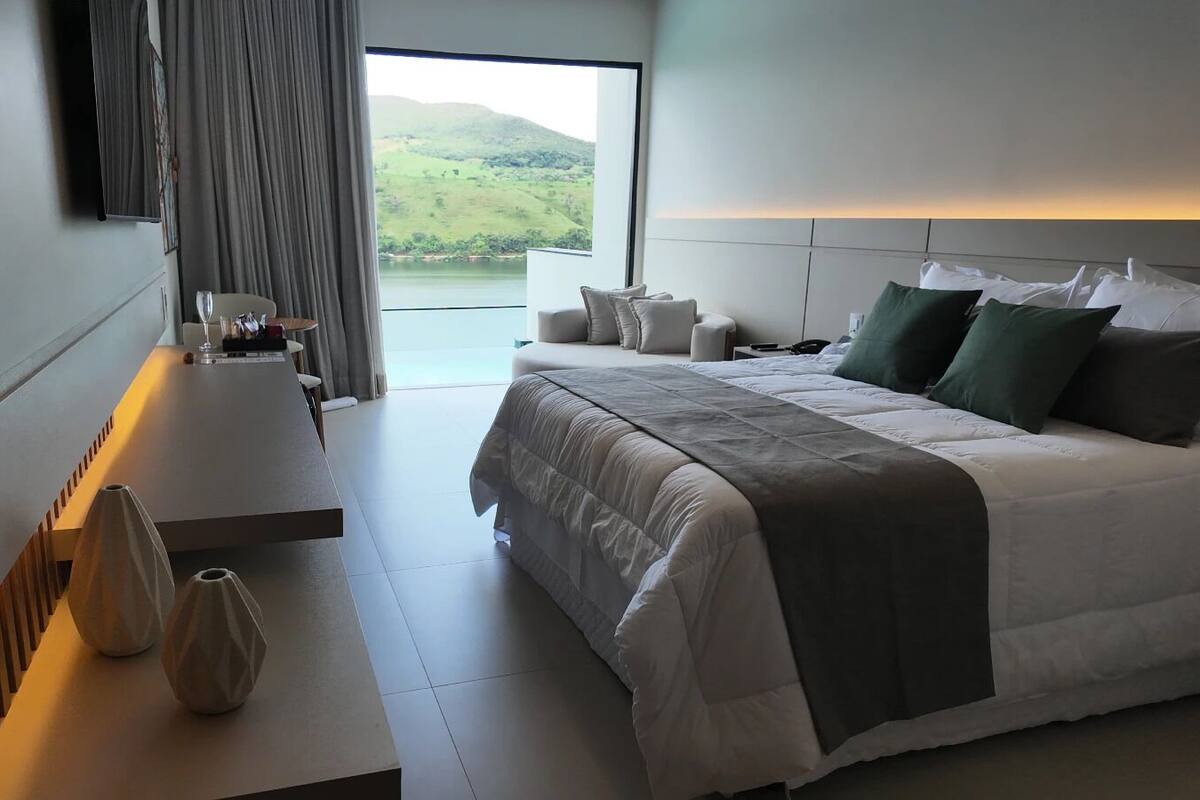 Una habitación de hotel moderna con una cama grande, una mesa de comedor y vistas al exterior.