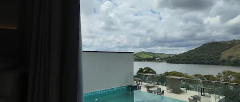A balcony with a glass edge pool, outdoor furniture, and a view of a lake and hills.