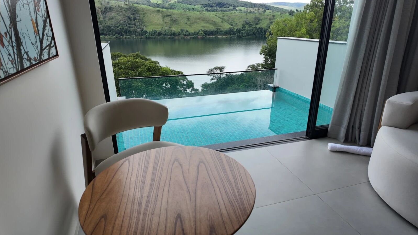 A modern room with a wooden table and a chair, a glass balustrade, and a view of a lake.