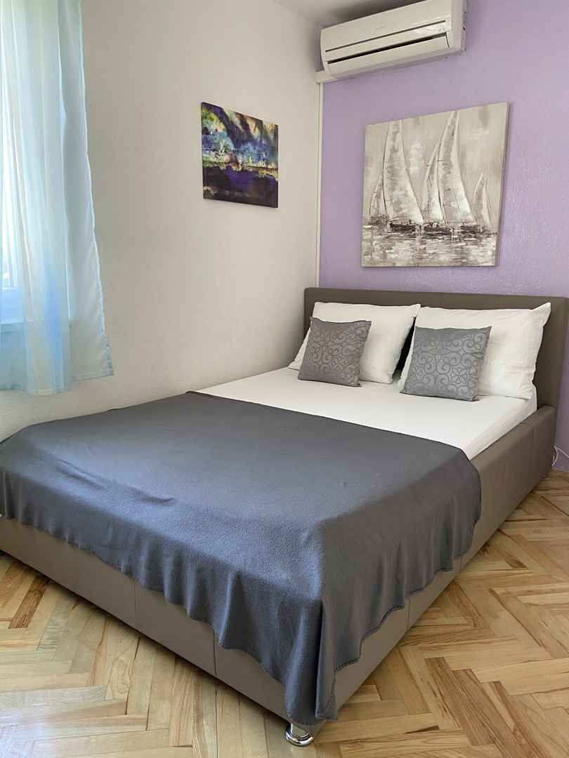 Un dormitorio con cama, ventana con cortinas, aire acondicionado y dos cuadros en la pared.
