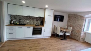 A compact kitchen with white cabinets, a built-in oven, and a dining area with two chairs. - Holiday apartment near the sea (Baška)