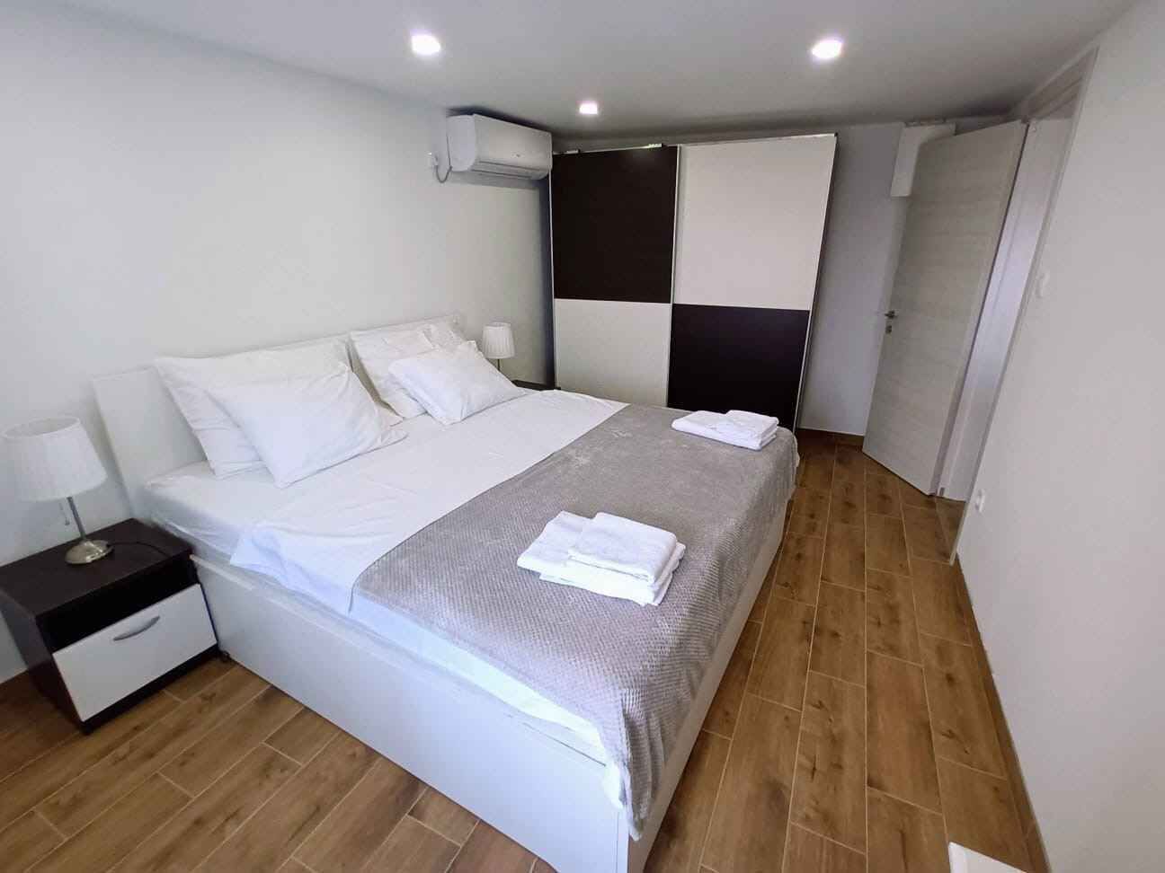 Una habitación de hotel moderna con una cama grande, una mesita de noche, un aire acondicionado instalado en la pared y una puerta que da a otra habitación.