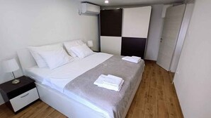 A modern hotel room with a large bed, a nightstand, a wall-mounted air conditioner, and a door leading to another room. - Holiday apartment near the sea (Baška)