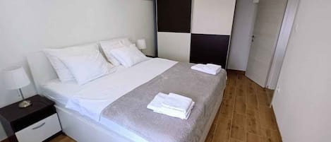 A modern hotel room with a large bed, a nightstand, a wall-mounted air conditioner, and a door leading to another room.