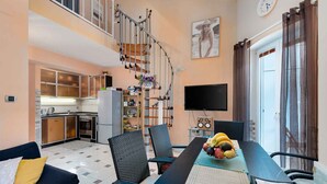 Een moderne woonkamer met een eettafel, stoelen, een bank, een trap, een keuken en een televisie.
