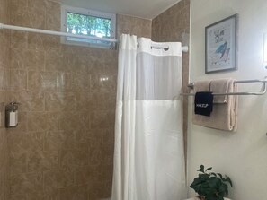 A bathroom with a shower curtain, a towel rack with towels, a framed picture, and a potted plant.