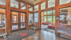 Een lobby met houten balken, een ruimte voor golfers of fietsers, een rode bank en een trolley.