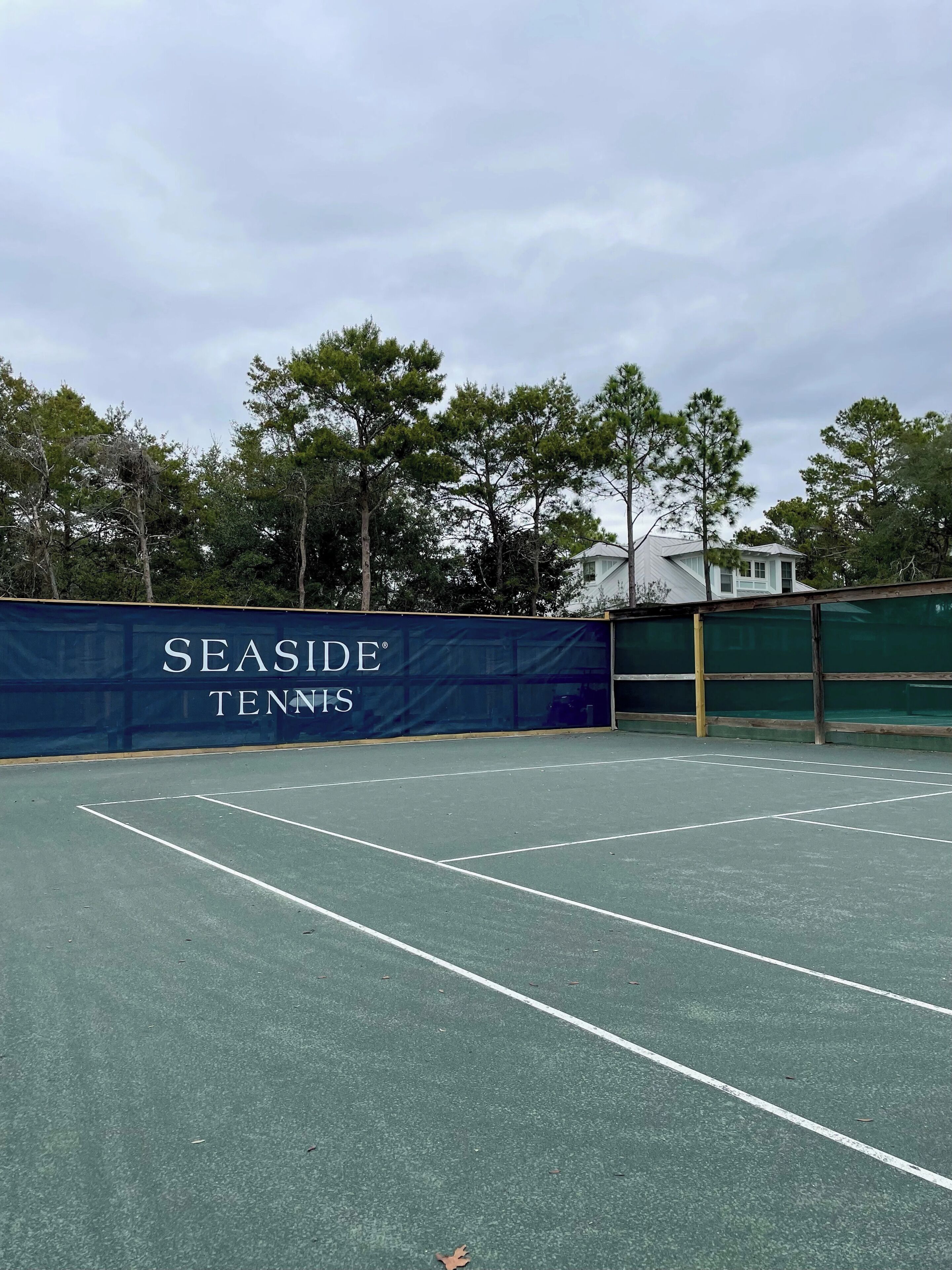 Een tennisbaan met een banner waarop 'SEASIDE TENNIS' staat, en een gebouw op de achtergrond.