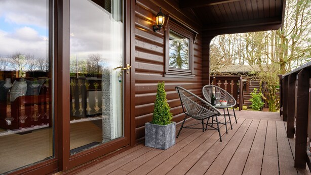 A wooden deck with a glass door, two chairs, and a small potted plant.