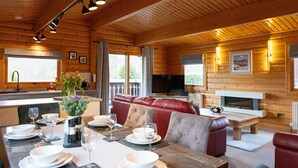 A wooden cabin interior with a dining area, a sofa, a fireplace, and a television.