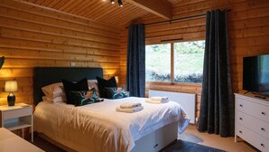 A wooden cabin bedroom with a bed, bedside table, and a TV.