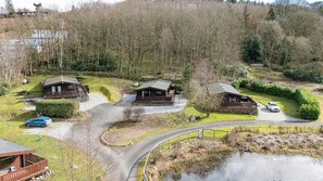 Een chaletgedeelte met meerdere houten chalets, een grindpad en een omliggend bos.