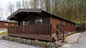 A wooden cabin with a balcony, stone foundation, and a gravel pathway.