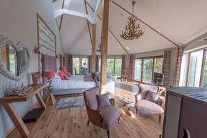 A spacious bedroom with a large bed, a sitting area with chairs, a wooden floor, and a view through large windows. - Silver Birch Treehouse -  a treehouse that sleeps 2 guests  in 0 bedrooms (Glenshee)