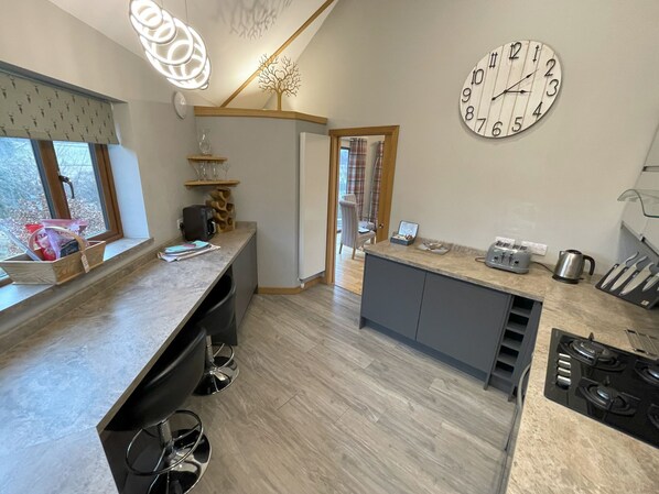 Una cocina moderna con una isla central, un reloj de pared grande y un comedor con vistas al exterior.