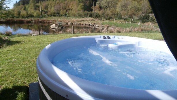 A hot tub with a view of a lake and forest. - Smiddy Cottage -  a cottage that sleeps 4 guests  in 2 bedrooms (Glenshee)