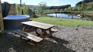A wooden picnic table and a hot tub in a garden with a pond and hills in the background. - Smiddy Cottage -  a cottage that sleeps 4 guests  in 2 bedrooms (Glenshee)