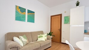 A living room with a beige sofa, a white dining table, and a wooden door.