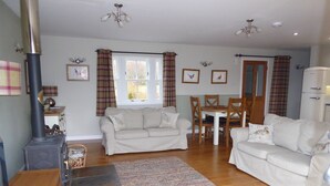 A cozy living room with a sofa set, a dining table with chairs, a fireplace, and a kitchen area. - Groose Hoose -  a cottage that sleeps 4 guests  in 2 bedrooms (Glenshee)