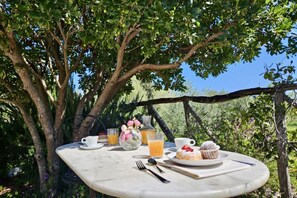 A table set outdoors with a glass of orange juice, a cup, a pastry, and a vase with flowers. - Green Hotel I Mandorli_Albergo Rurale (Orosei)