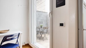 A room with a white desk, a blue chair, a small table with a plant, and a door with a sign. - Hostmate - Milano - Piazza Mentana (Milan)