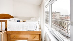 A bedroom with a wooden bed, a window with a view of buildings, and a white wall. - Hostmate - Milano - Piazza Mentana (Milan)