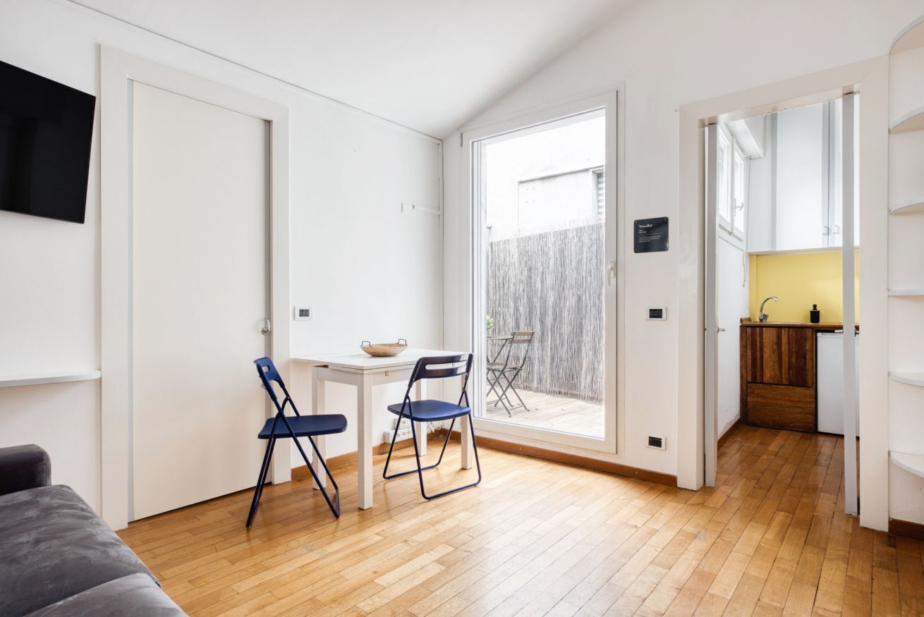 Un espace de vie compact comprenant un coin repas, une petite cuisine et une porte-fenêtre coulissante donnant sur un jardin.