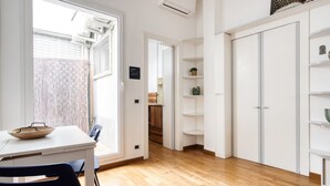 A modern kitchen with white cabinetry, a dining table with chairs, and a view through an open door to a balcony. - Hostmate - Milano - Piazza Mentana (Milan)