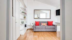 A room with a grey sofa, a white cabinet, a mirror, and a wooden floor. - Hostmate - Milano - Piazza Mentana (Milan)