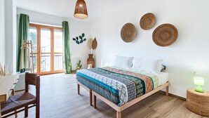 A modern bedroom with a wooden bed, a desk, and a chair. There are woven wall hangings and a green curtain. - 7Rooms - The Countryside (Lecce)