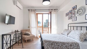 A bedroom with a bed, a desk, a chair, and a sofa. There is a window with curtains, a wall-mounted TV, and framed pictures. - 7Rooms - The City-Lecce Selection (Lecce)