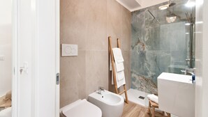 A modern bathroom with a bidet, a glass shower enclosure, and a marble wall.