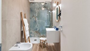 A modern bathroom with a glass shower enclosure, a white sink, and a wooden stool.