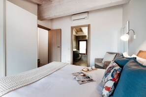 A hotel room with a bed, a reading area, a sofa, and a small table with a magazine and pastries.